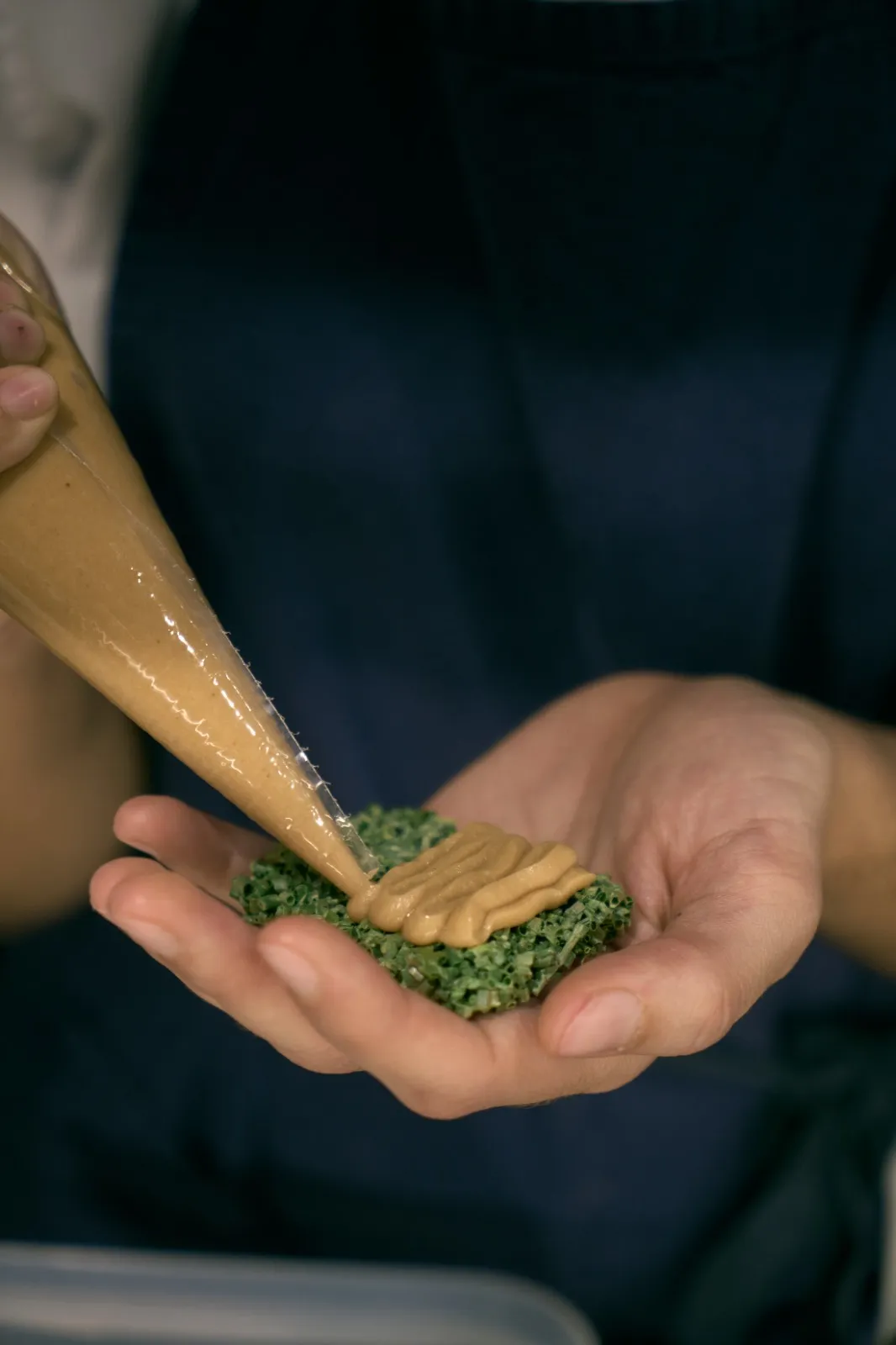 Rellenando con manga pastelera un bocado de bizcocho verde sostenido en la mano.
